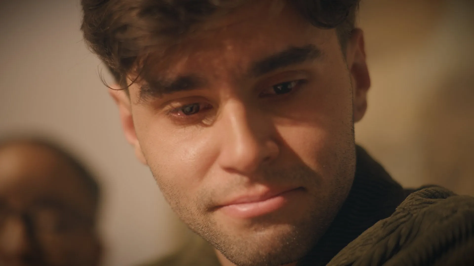 Close-up of a young man with tears in his eyes, softly smiling.