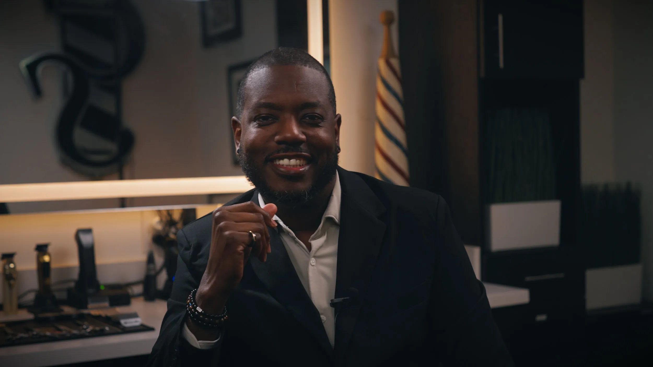 Smiling salon owner in a dark suit seated in a styling chair during an interview.
