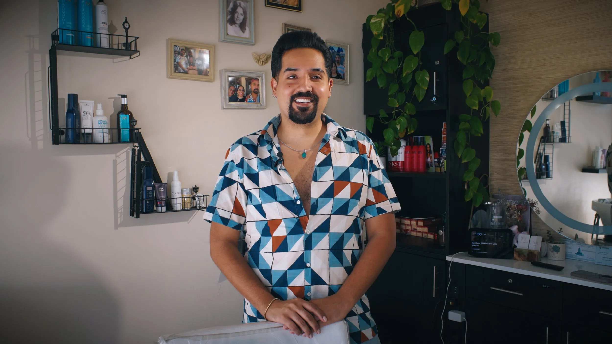 Smiling stylist in a geometric-print shirt standing in his bright salon suite.