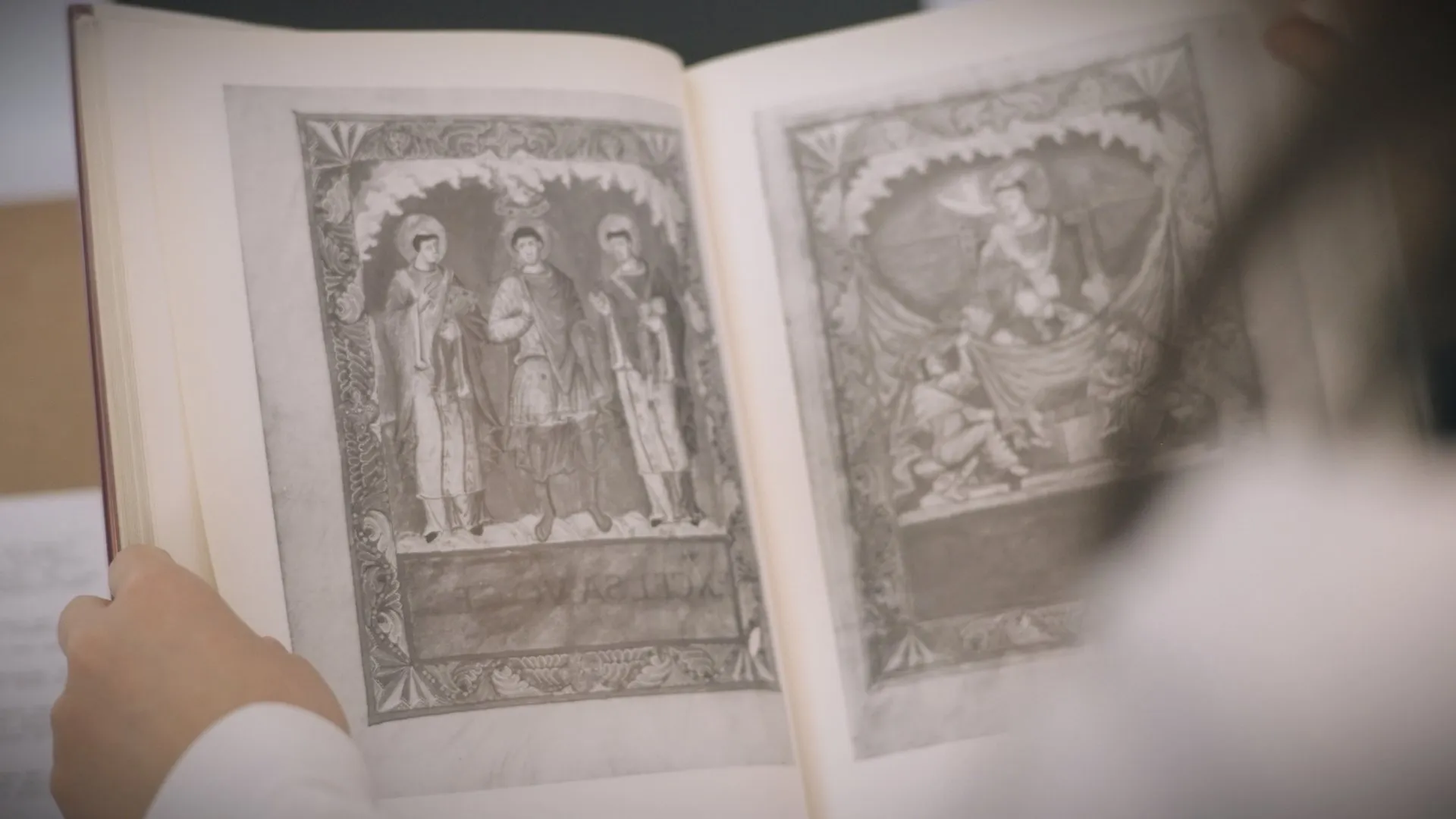 Hands turning the pages of an illuminated historical manuscript.