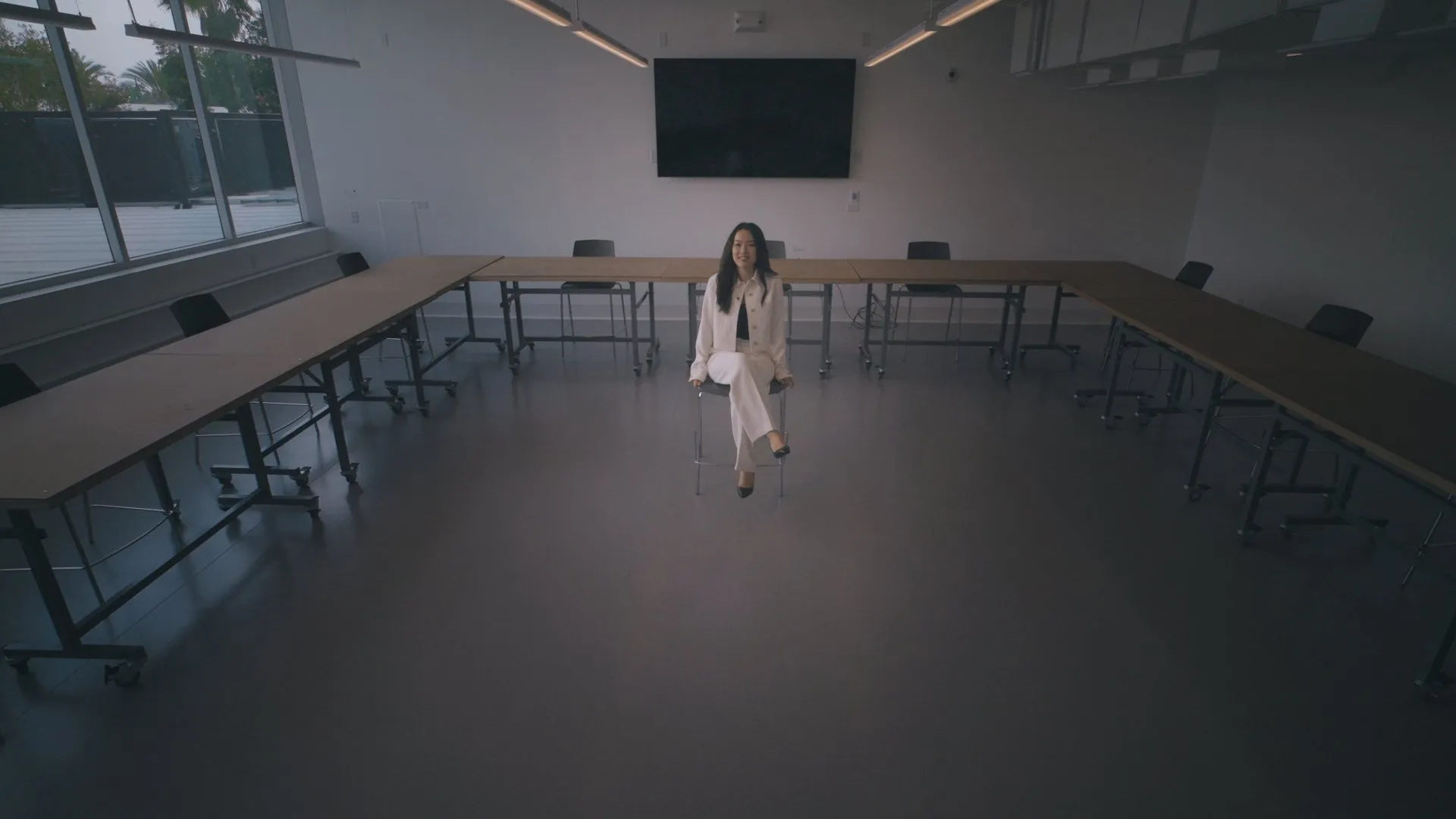 A woman in white walks alone through a large, empty conference room.